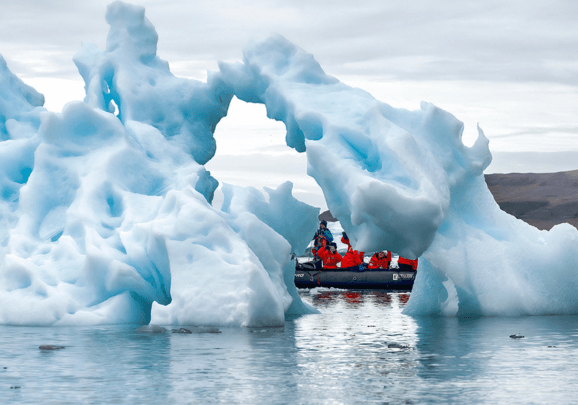 Ein Schlauchboot mit Kreuzfahrt-Gästen fährt in Grönland vorbei an Eisbergen